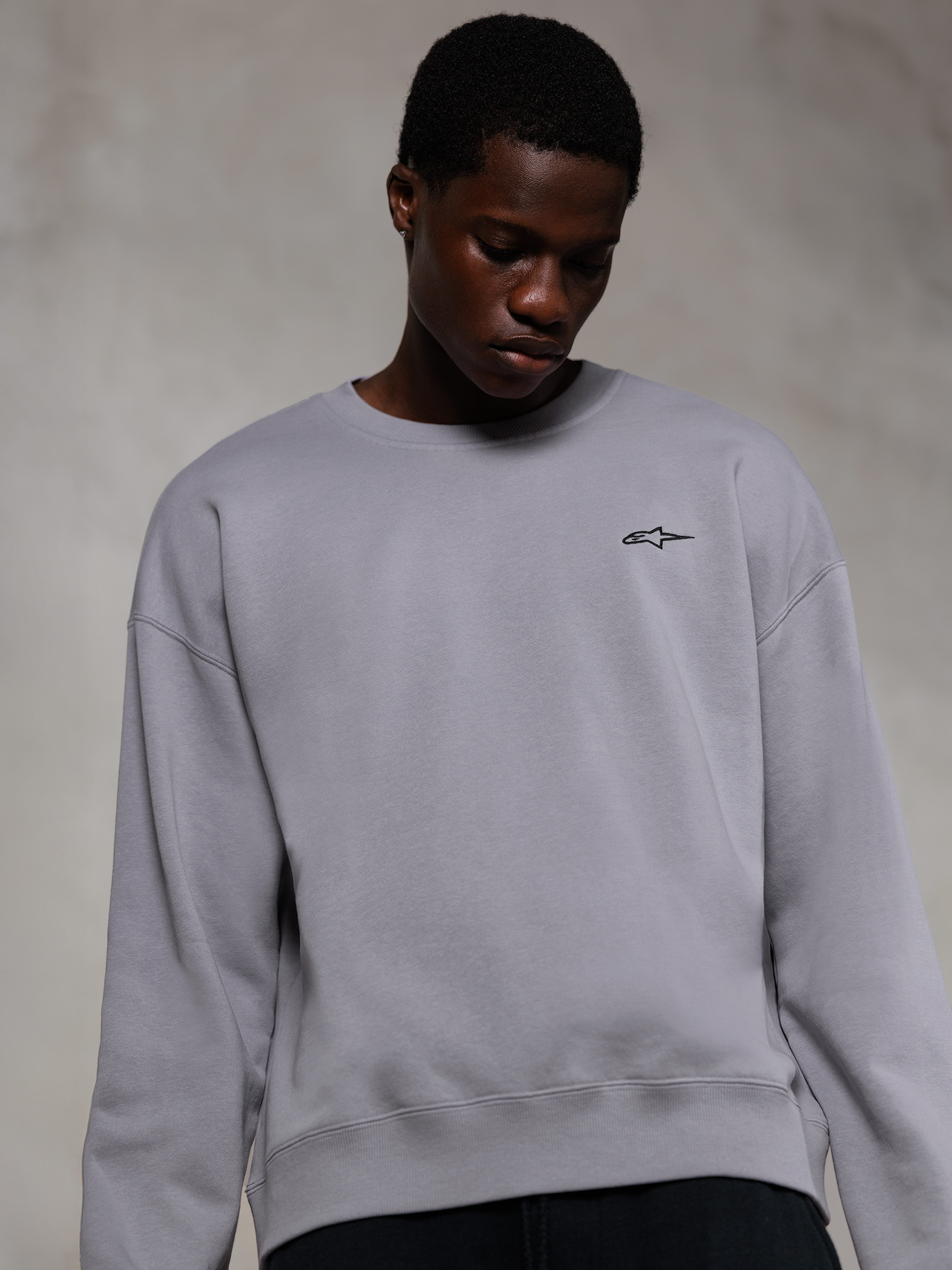 Alpinestars Essentials Ageless Crew, sweatshirt premium de gola redonda prateada, com um pequeno logótipo Alpinestars preto no peito, vestida por um modelo, estilo casual streetwear com textura suave de fleece