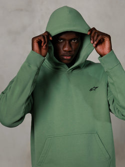 Alpinestars Essentials Ageless Hoodie, streetwear casual, verde cacto com pequeno logótipo preto no peito, modelo a usar o hoodie com o capuz colocado, bolso canguru frontal, design descontraído inspirado no desporto motorizado