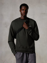 Alpinestars Essentials Ageless Crew, sweatshirt de gola redonda, cor Off Black, com um pequeno logótipo branco da Alpinestars no peito, gola e bainha caneladas, modelo masculino com alça de mala a tiracolo, estilo casual lifestyle streetwear