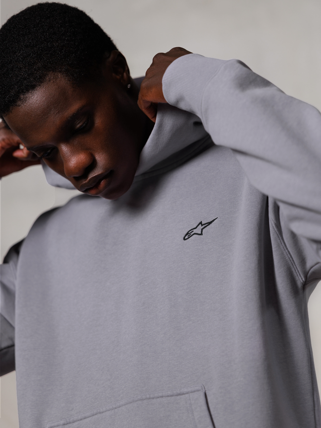 Alpinestars Essentials Ageless Hoodie, Silver, grande plano de um homem a ajustar o capuz da sweatshirt cinzenta, pequeno logótipo preto Alpinestars no peito, vestuário casual premium inspirado no desporto motorizado