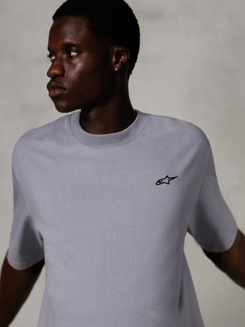 Modelo a usar Alpinestars Essentials Ageless SS Tee, t-shirt de manga curta, prateada, com um pequeno logótipo preto no peito, corte relaxado, design de streetwear simples e minimalista