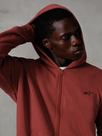 Alpinestars Essentials Ageless Zip Hoodie, vermelho tijolo, streetwear casual lifestyle, capuz levantado com a mão atrás da cabeça, pequeno logótipo Astars preto no peito, hoodie em fleece de corte descontraído
