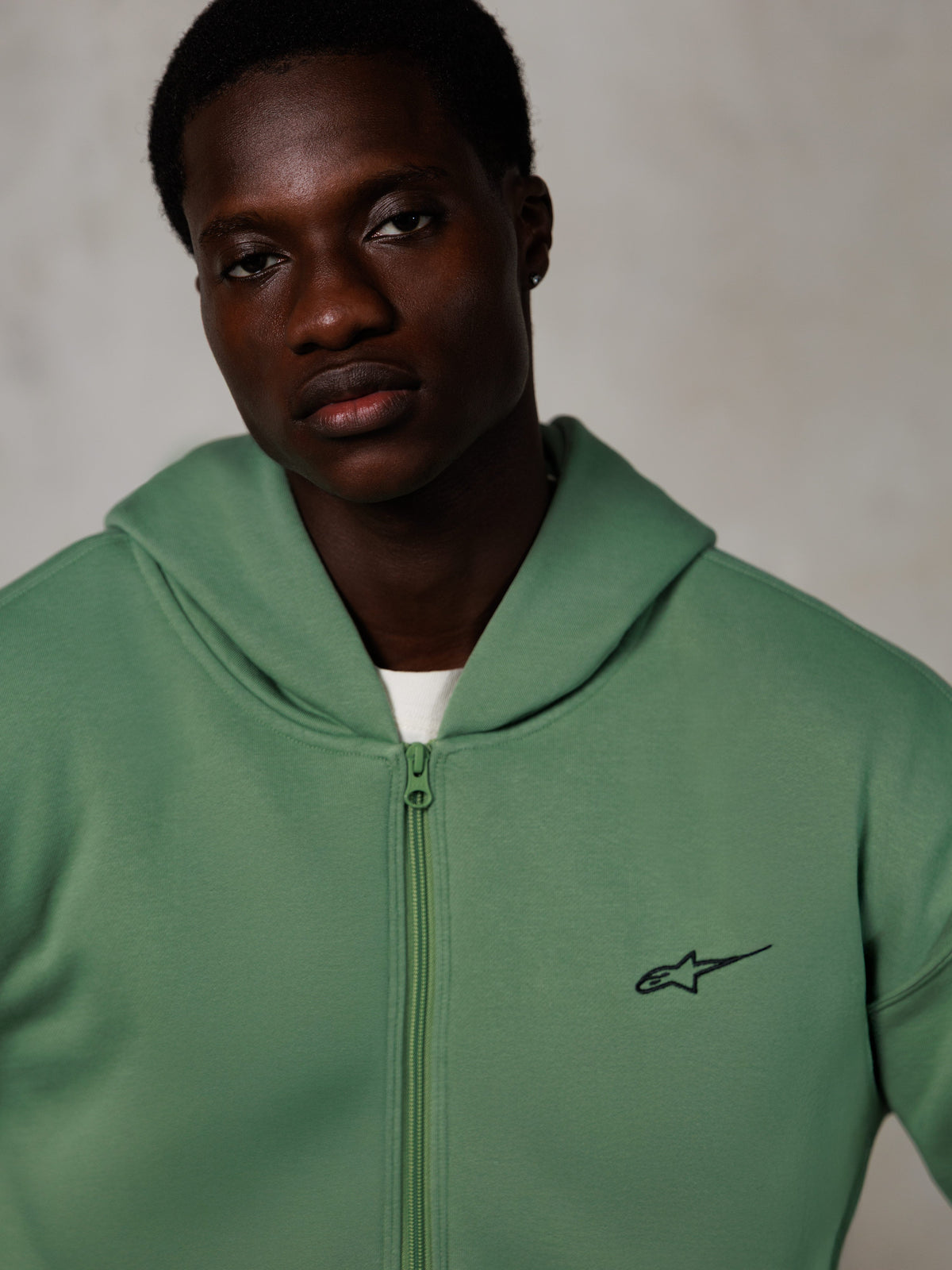 Alpinestars Essentials Ageless Zip Hoodie, retrato lifestyle, verde cactus com pequeno logótipo preto, fecho de correr frontal, textura de fleece suave, streetwear casual inspirado no desporto motorizado
