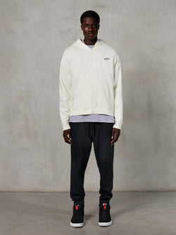 Alpinestars Essentials Ageless Zip Hoodie, streetwear casual, off-white com logótipo preto subtil no peito, fecho de correr frontal integral, design com capuz, corte relaxado, combinado com calças de fato de treino pretas e sapatilhas