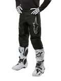 Alpinestars 2024 Fluid Graphite Pants, Motocross Pants, Black and Silver, featuring a silver Alpinestars logo on the thigh, shown worn with white motocross boots and gloves, designed for off-road motorcycle racing