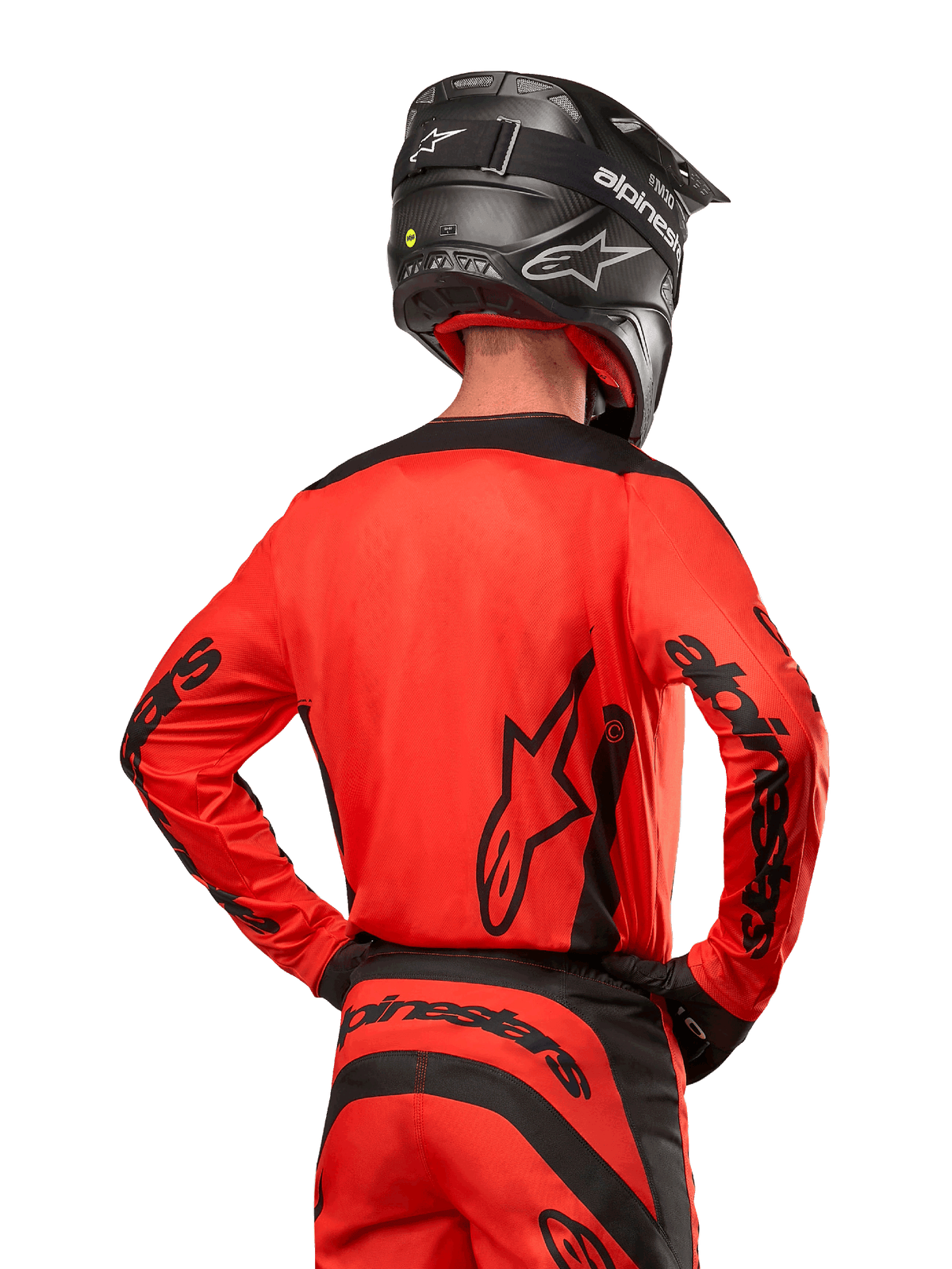 Piloto de motocross visto de costas a usar a camisola Alpinestars 2024 Fluid Lurv em Hot Orange e Preto, com marca Alpinestars em destaque nas costas e mangas, combinada com calças de motocross a condizer e um capacete preto, concebida para performance em competição off-road.