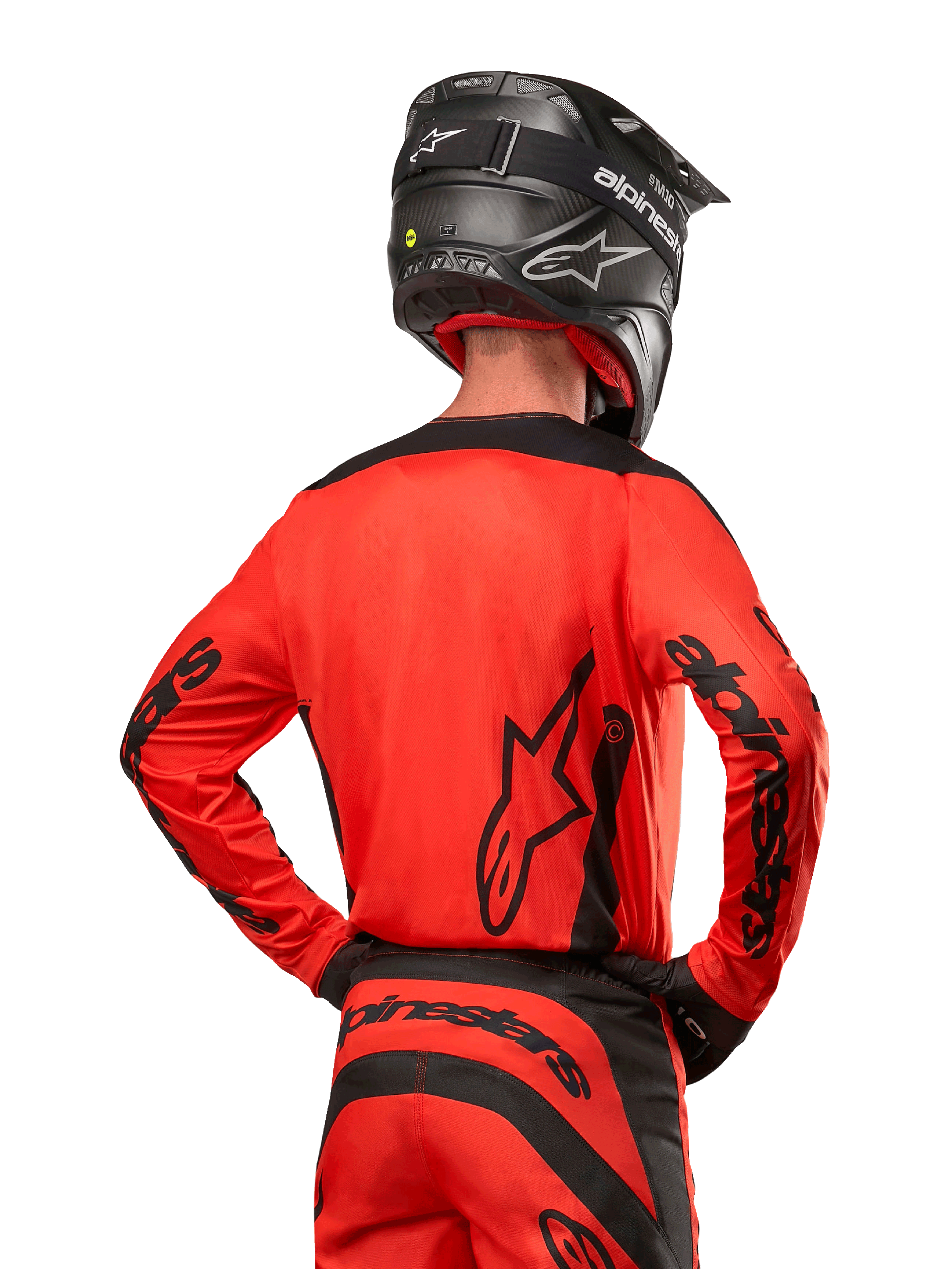 Piloto de motocross visto de costas a usar a camisola Alpinestars 2024 Fluid Lurv em Hot Orange e Preto, com marca Alpinestars em destaque nas costas e mangas, combinada com calças de motocross a condizer e um capacete preto, concebida para performance em competição off-road.