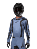 Piloto de motocross a usar a camisola Alpinestars 2024 Fluid Lurv, azul claro e preto, combinada com capacete e óculos pretos, com detalhes gráficos pretos e o logótipo de estrela da Alpinestars, equipamento de performance para corridas todo-o-terreno