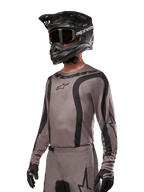 Alpinestars 2024 Fluid Lurv Jersey, Motocross Jersey, Mud Black and Gray, long-sleeve design with curved black stripes and logos, worn with matching pants and a black motocross helmet, coordinated off-road racing setup