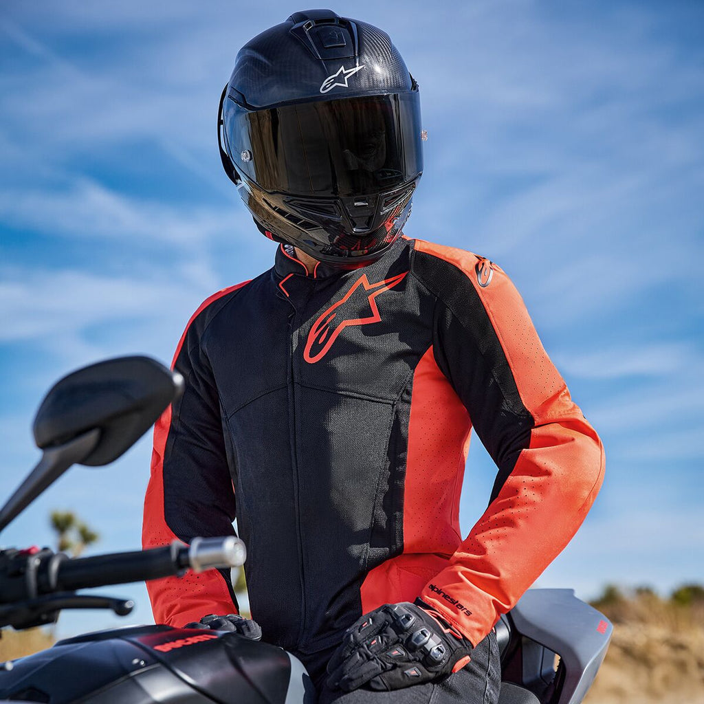 Casaco Alpinestars Viper Air V4 em Vermelho Fluo e Preto, usado por um motociclista numa mota, com um logótipo grande no peito e painéis de malha ventilada, combinado com um capacete de fibra de carbono e luvas pretas, equipamento de motociclismo de estrada e desportivo