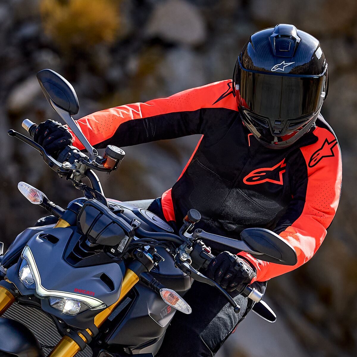 Casaco Alpinestars Viper Air V4, Vermelho Fluo e Preto, usado por um motociclista inclinado numa curva numa mota desportiva, capacete integral preto e luvas, equipamento de alta performance para competição e condução desportiva