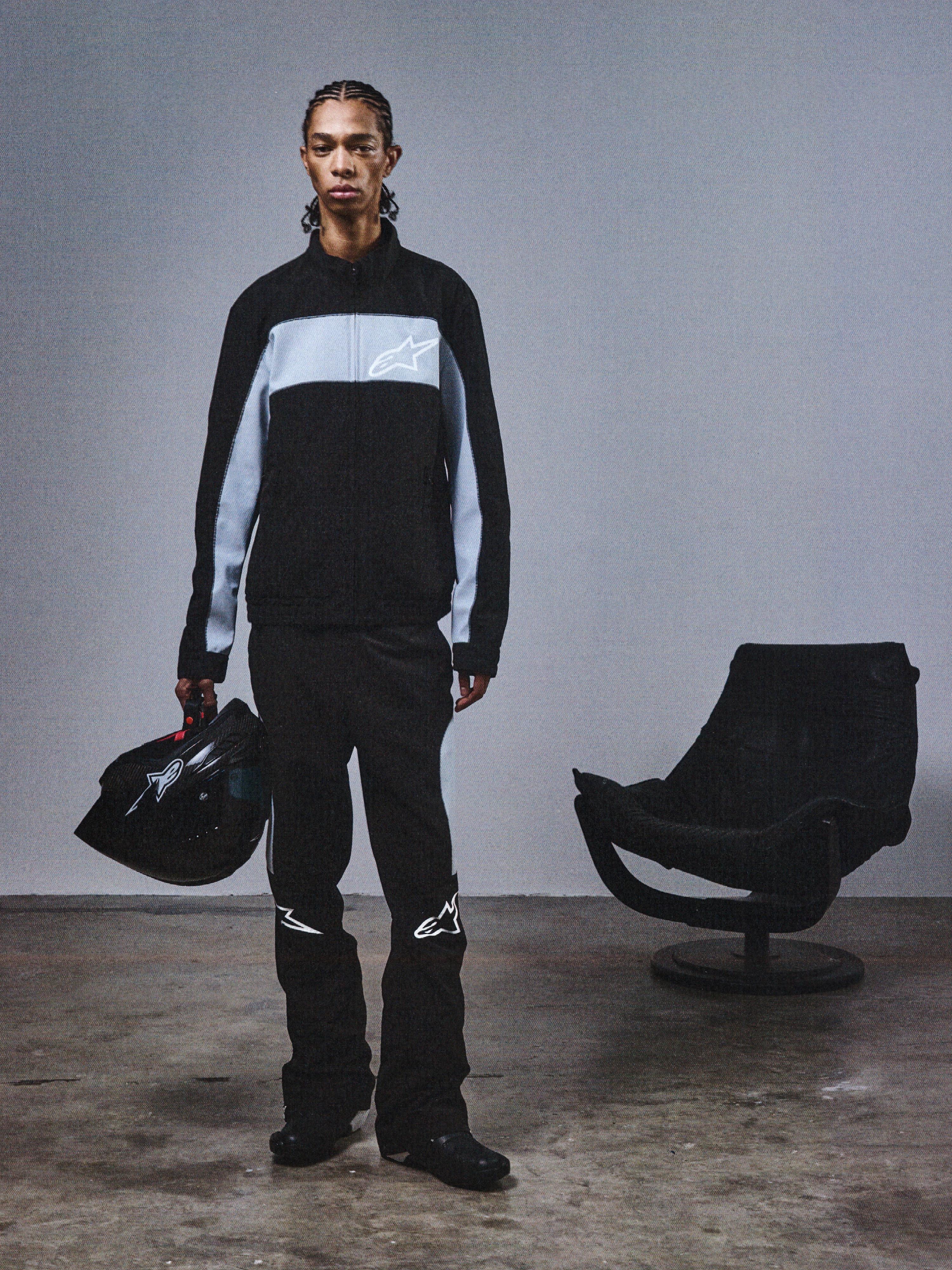Alpinestars RSRV Track Jacket, casaco desportivo preto e cinzento com logótipo de estrela, pessoa com capacete a condizer, estilo urbano minimalista, coleção streetwear premium