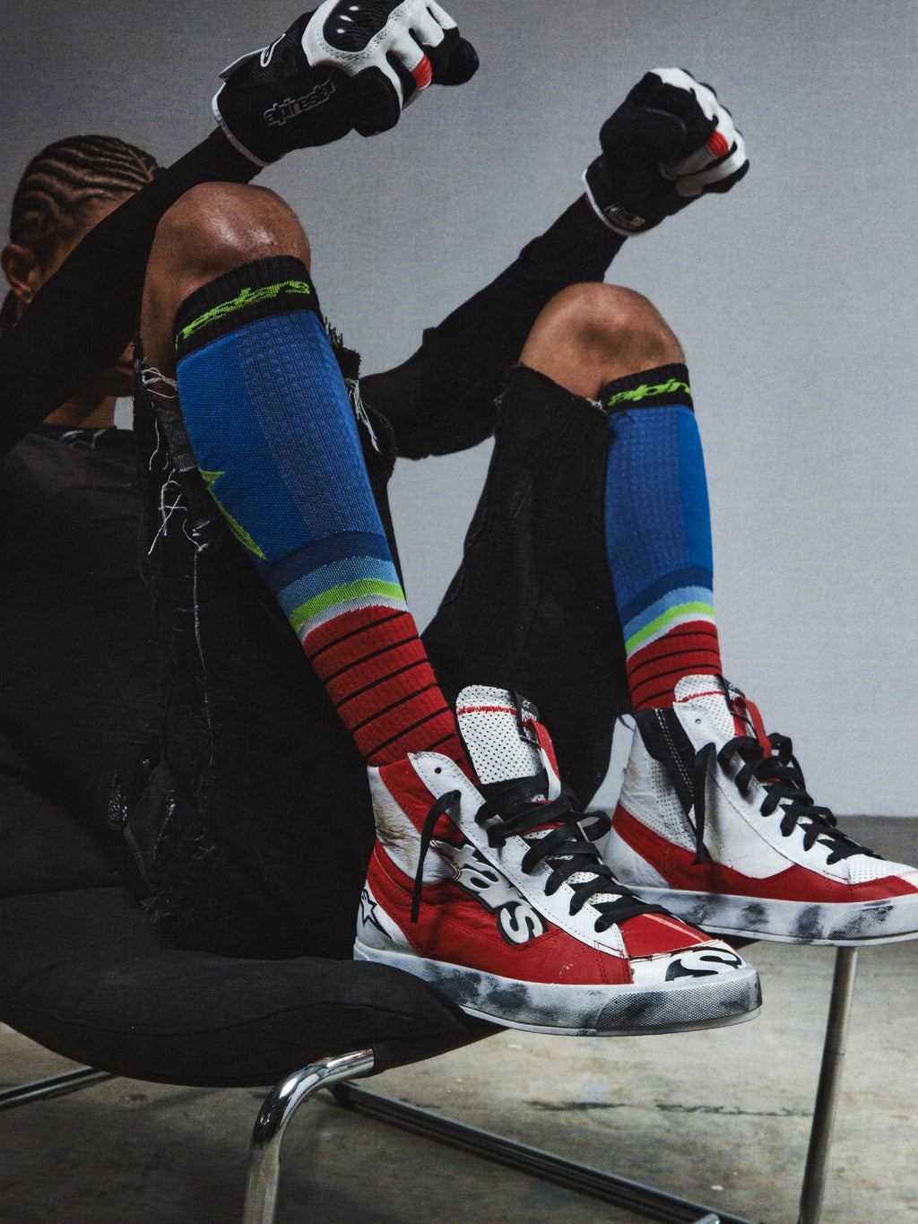 Alpinestars RSRV Legacy Shoe, sapatilhas altas vermelhas, brancas e pretas, estilo streetwear premium, pessoa sentada com meias coloridas às riscas, luvas pretas com detalhes vermelhos e brancos