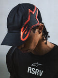 Alpinestars RSRV Lowside Hat, boné preto com design de chamas vermelhas e pretas, estilo streetwear premium, vista frontal com pessoa a usar