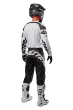 Equipamento completo de motocross Alpinestars visto de costas, incluindo calças 2024 Racer Hana pretas e brancas com logótipo, camisola branca, capacete preto e botas brancas, vestuário técnico para pilotagem off-road