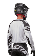 Camisola Alpinestars 2024 Racer Hana, branca e preta, vista traseira mostrando o ajuste ergonómico e logótipos de destaque nas mangas, combinada com um capacete de motocross preto e calças pretas e brancas a condizer, equipamento de alta performance para condução off-road