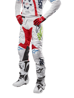 Calças Alpinestars Racer Hana 2024, calças de motocross para corrida, brancas com detalhes em vermelho, azul e verde lima, com design protetor e painéis de pele nos joelhos, usadas com camisola a condizer, luvas vermelhas e botas brancas com fivelas, equipamento desportivo de desportos motorizados