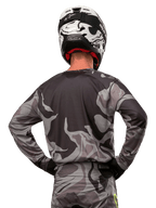Alpinestars 2024 Racer Tactical Jersey, camisola de motocross, Cast Gray Camo Magnet, vista traseira com padrão de camuflagem cinzento e preto, usada com calças a condizer e um capacete preto e branco, equipamento profissional de corrida para todo-o-terreno