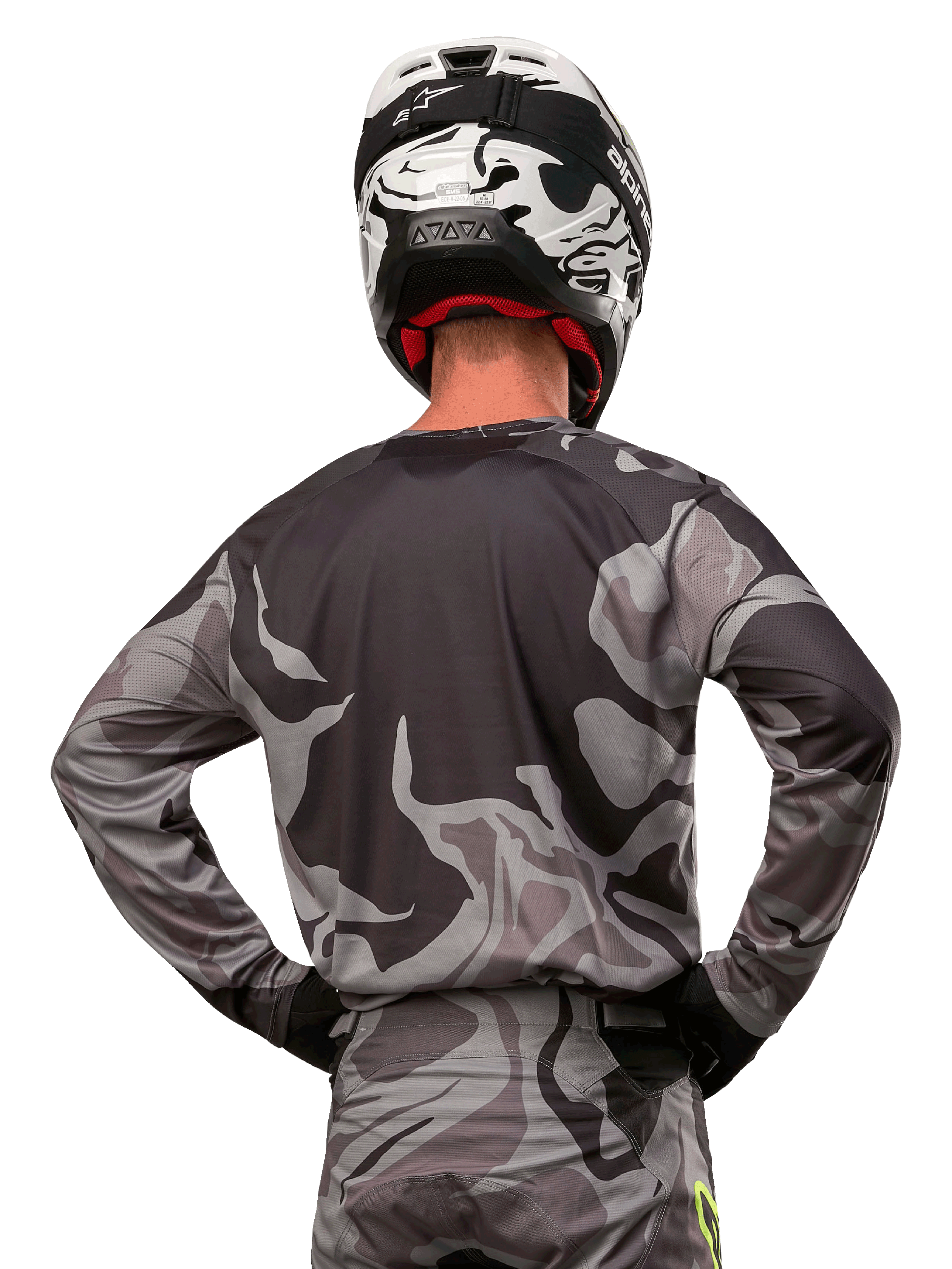 Alpinestars 2024 Racer Tactical Jersey, camisola de motocross, Cast Gray Camo Magnet, vista traseira com padrão de camuflagem cinzento e preto, usada com calças a condizer e um capacete preto e branco, equipamento profissional de corrida para todo-o-terreno