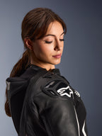 Mulher a usar o Fato de Cabedal de 2 Peças Alpinestars Stella GP-R7, vista em grande plano do ombro em pele preta com proteção DFS RR e logótipo de estrela branca, apresentando a corcova aerodinâmica integrada e detalhes perfurados.