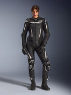 Mulher a usar o Fato de Cabedal Alpinestars Stella GP-R7 de 2 Peças em preto com detalhes brancos, com painéis de pele perfurada e logótipos brancos no peito e nos joelhos, combinado com luvas e botas de corrida pretas a condizer, equipamento profissional de motociclismo