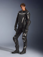 Mulher a usar o fato de cabedal Alpinestars Stella GP-R7 de 2 peças em preto, equipamento profissional de corrida de motociclismo com detalhes e logótipos em branco, combinado com luvas e botas de corrida pretas, fotografia de estúdio de corpo inteiro