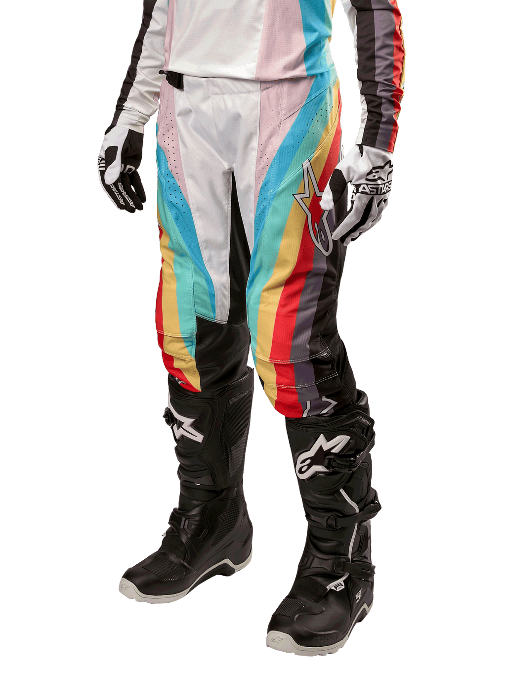 Calças Alpinestars Stella Techstar 2024 para Mulher, calças de motocross, pretas multicor com riscas diagonais vermelhas, amarelas e azuis, usadas com botas de condução pretas e luvas brancas, com painéis de proteção pretos nos joelhos e logótipo de destaque para corridas de todo-o-terreno.