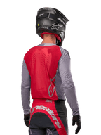 Piloto de motocross visto de costas a usar a camisola Alpinestars Supertech Dade 2024 em Iron Red Berry e cinzento, com painel traseiro em malha respirável, pormenores do logótipo em prateado, capacete preto e calças de corrida a condizer para desempenho profissional em todo-o-terreno