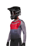 Alpinestars 2024 Supertech Dade Jersey, camisola de motocross, vermelha Iron Red Berry e cinzenta, manga comprida com perfurações cortadas a laser, usada por um piloto com capacete preto e luvas pretas, corte de corrida atlético profissional