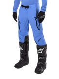 Alpinestars 2024 Supertech Dade Pants, calças de motocross, azul claro com logótipos gráficos pretos, com perfurações de ventilação e fivela magnética na cintura, combinadas com botas e luvas técnicas pretas, equipamento profissional de corrida todo-o-terreno
