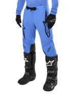 Alpinestars 2024 Supertech Dade Pants, calças de motocross, azul claro com logótipos gráficos pretos, com perfurações de ventilação e fivela magnética na cintura, combinadas com botas e luvas técnicas pretas, equipamento profissional de corrida todo-o-terreno