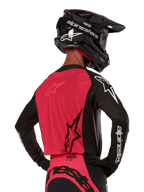 Alpinestars 2024 Supertech Ward Jersey, camisola de motocross, preto e vermelho berry, vista traseira com painel de malha vermelho e mangas pretas com logótipos brancos, usada com capacete de fibra de carbono preto e luvas, ajuste de corrida atlético para condução todo-o-terreno
