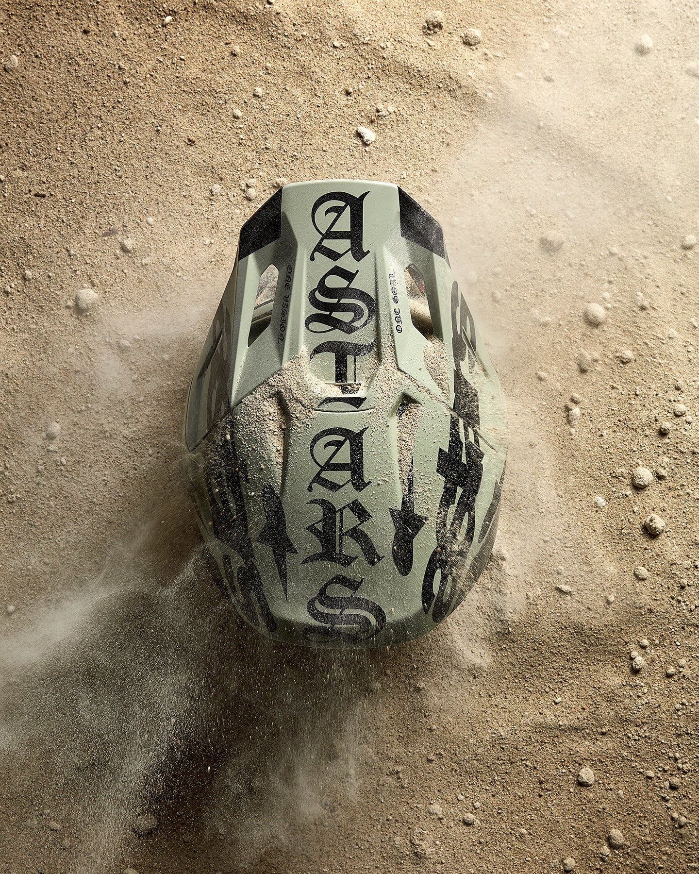 Alpinestars S-M7 Wolf Dust Helmet, Motocross Racing, Dune Black with gothic ASTARS logo, shown in desert sand.
