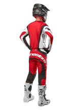 Calças Alpinestars Techstar Ocuri 2024, calças de motocross, Mars Red White Black, vista traseira de um piloto de motocross com equipamento de corrida completo, incluindo camisola a condizer, capacete preto e botas brancas e pretas, destacando a marca Alpinestars e a construção em tecido durável.