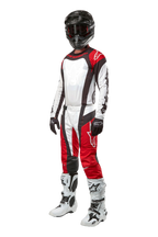 Piloto de motocross com equipamento completo Alpinestars, Calças Techstar Ocuri 2024 em Mars Red White Black, camisola a condizer, capacete preto com óculos, luvas pretas e brancas e botas de motocross brancas, conjunto profissional de corrida todo-o-terreno
