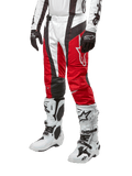 Alpinestars 2024 Techstar Ocuri Pants, calças de motocross, vermelho Mars, branco e preto, usadas com camisola branca e preta a condizer, luvas pretas e botas de corrida brancas com fivelas, equipamento de proteção técnico apresentado sobre um fundo branco