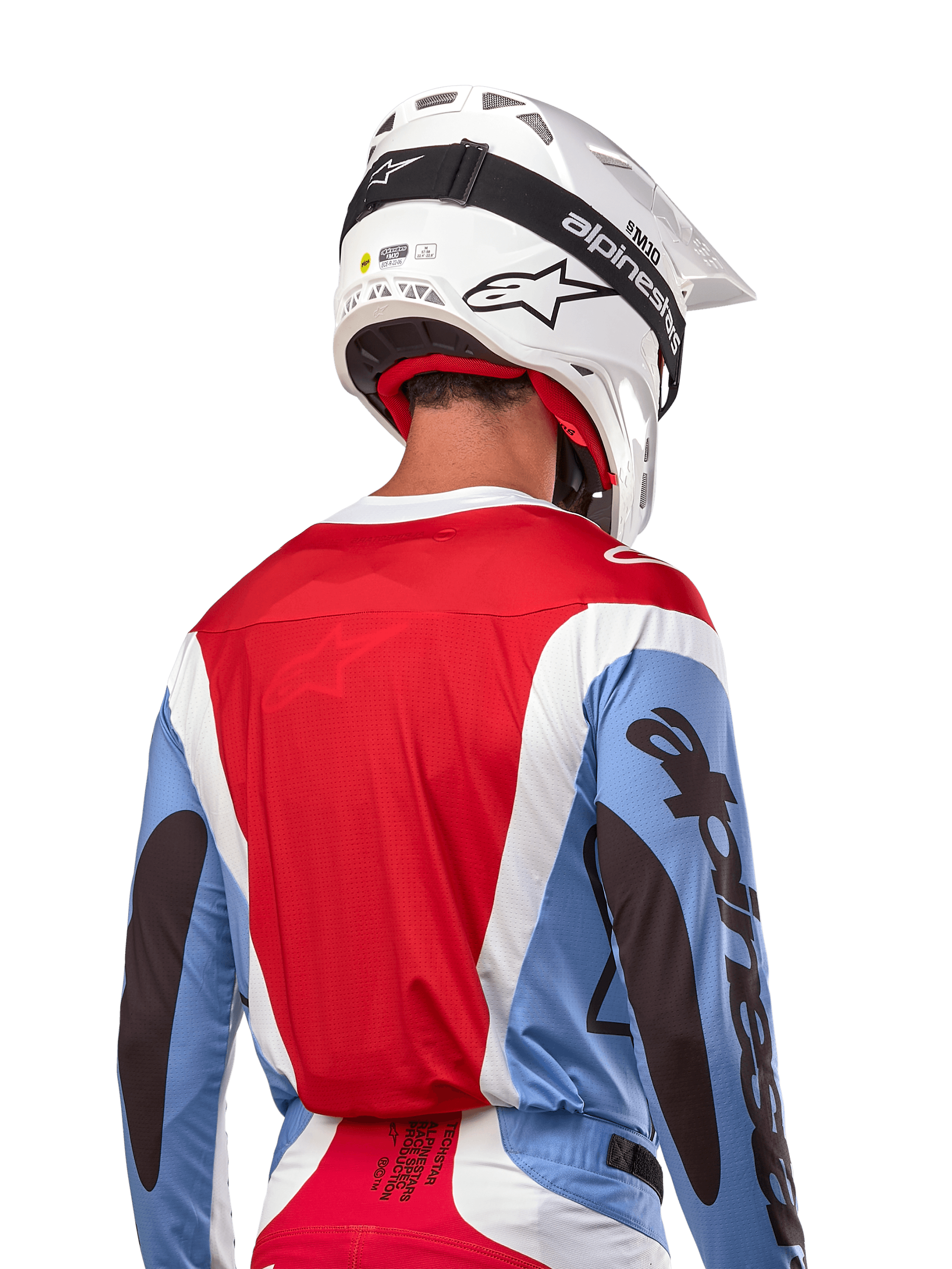 Camisola Alpinestars Techstar Ocuri 2024, camisola de motocross, azul claro, vermelho Mars e branco, vista traseira do piloto com capacete branco e óculos pretos, apresenta logótipos pretos de destaque nas mangas e corte ergonómico de corrida para performance em todo-o-terreno.