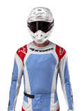 Camisola Alpinestars Techstar Ocuri 2024, camisola de motocross, azul claro, vermelho Mars e branco, vista frontal com ventilação cortada a laser e ajuste atlético, usada com capacete branco e óculos para um visual profissional de corrida todo-o-terreno