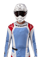 Camisola Alpinestars Techstar Ocuri 2024, camisola de motocross, azul claro, vermelho Mars e branco, vista frontal com ventilação cortada a laser e ajuste atlético, usada com capacete branco e óculos para um visual profissional de corrida todo-o-terreno