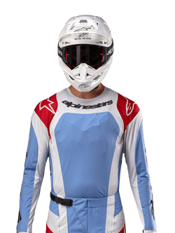 Camisola Alpinestars Techstar Ocuri 2024, camisola de motocross, azul claro, vermelho Mars e branco, vista frontal com ventilação cortada a laser e ajuste atlético, usada com capacete branco e óculos para um visual profissional de corrida todo-o-terreno