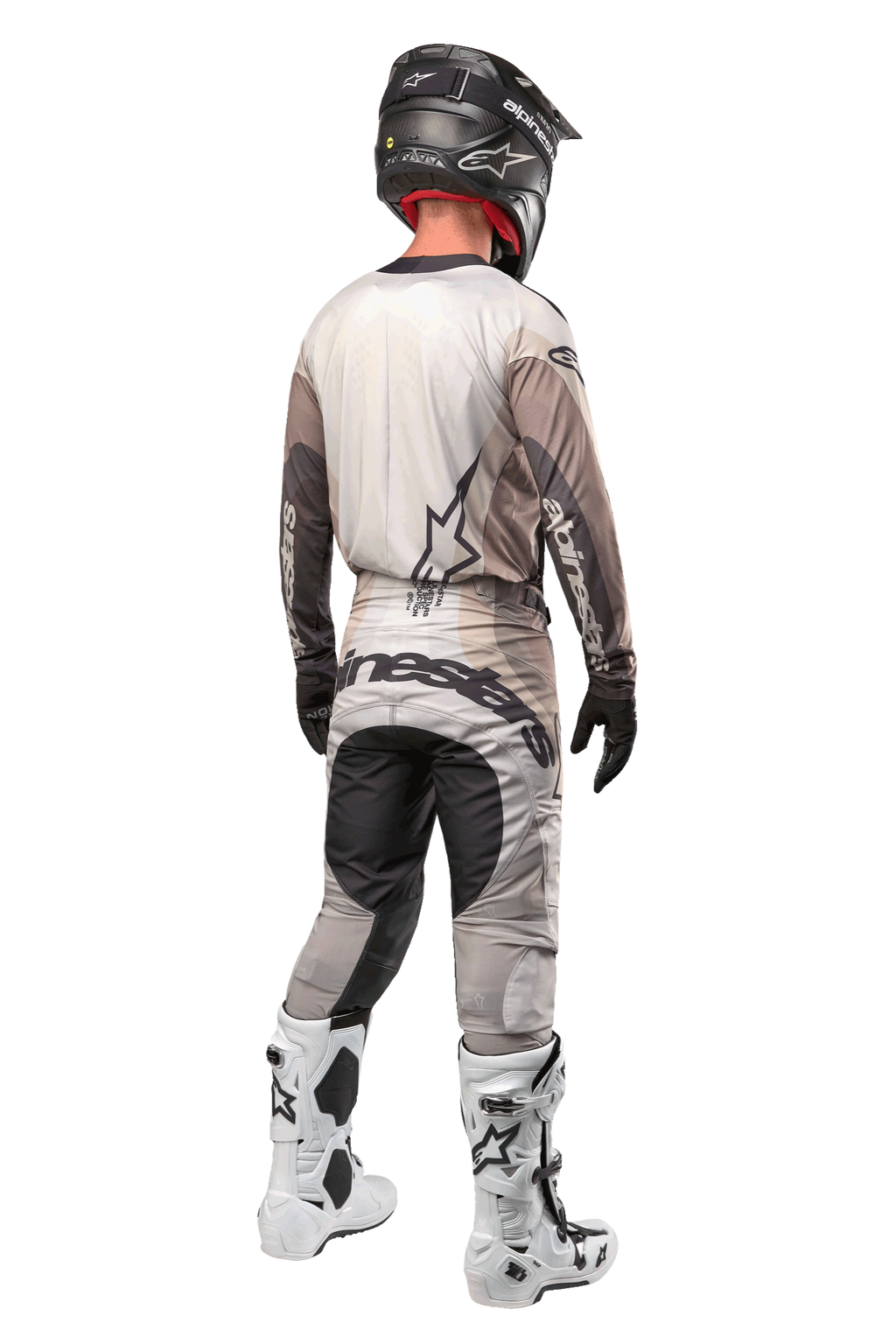 Alpinestars 2024 Techstar Pneuma Pants, calças de motocross, Areia Escura e Cinzento Iron Dust, vista traseira usada por um piloto com uma camisola a condizer, botas brancas e pretas e um capacete preto, com logótipo Alpinestars proeminente no assento e painéis escuros reforçados