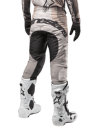 Alpinestars 2024 Techstar Pneuma Pants, calças de motocross, Areia Escura e Cinzento Poeira de Ferro, vista traseira da cintura para baixo, logótipo Alpinestars a preto no assento, usadas com botas de motocross brancas e pretas e luvas pretas, design durável de corte de corrida para competição todo-o-terreno
