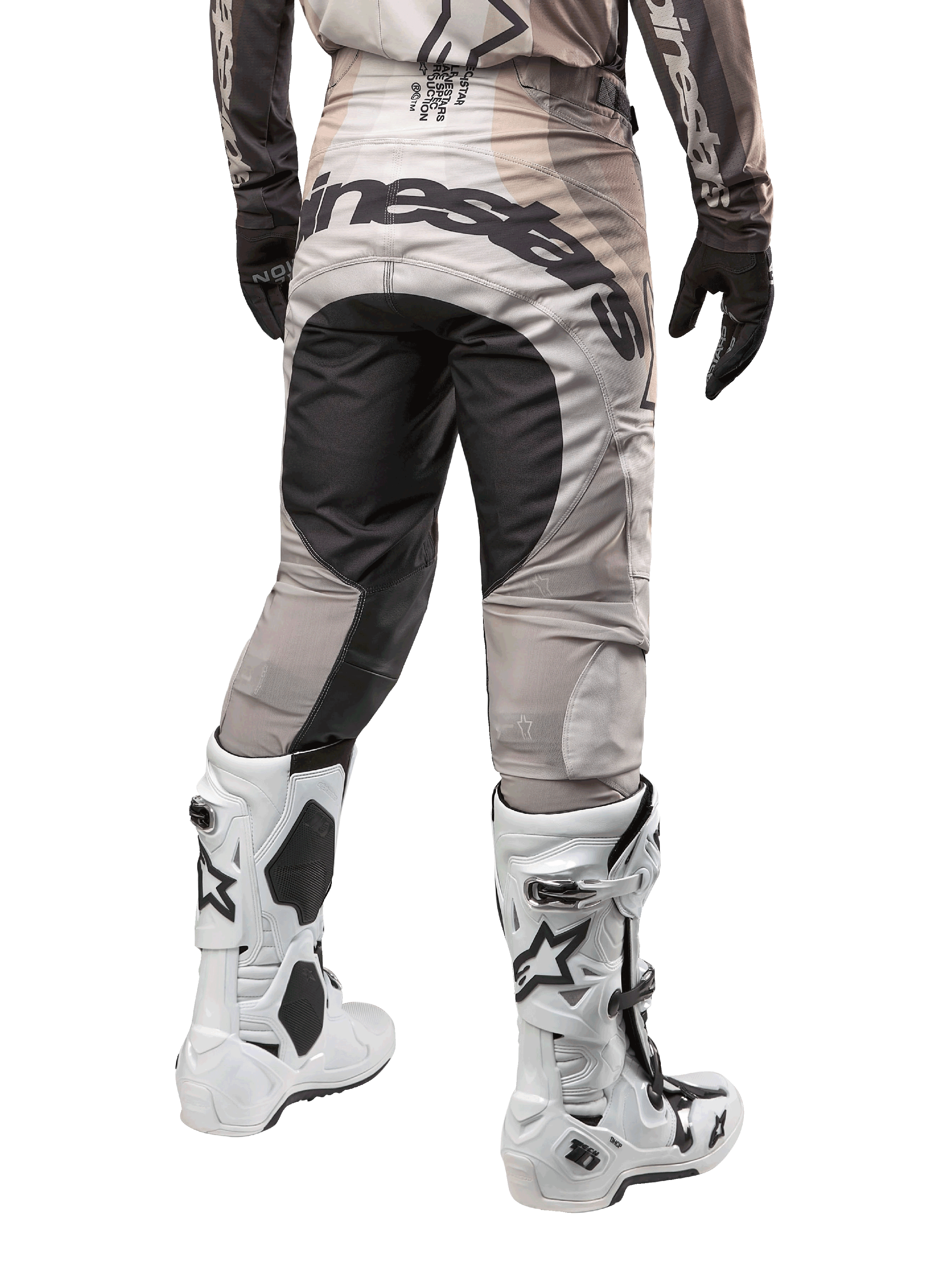 Alpinestars 2024 Techstar Pneuma Pants, calças de motocross, Areia Escura e Cinzento Poeira de Ferro, vista traseira da cintura para baixo, logótipo Alpinestars a preto no assento, usadas com botas de motocross brancas e pretas e luvas pretas, design durável de corte de corrida para competição todo-o-terreno