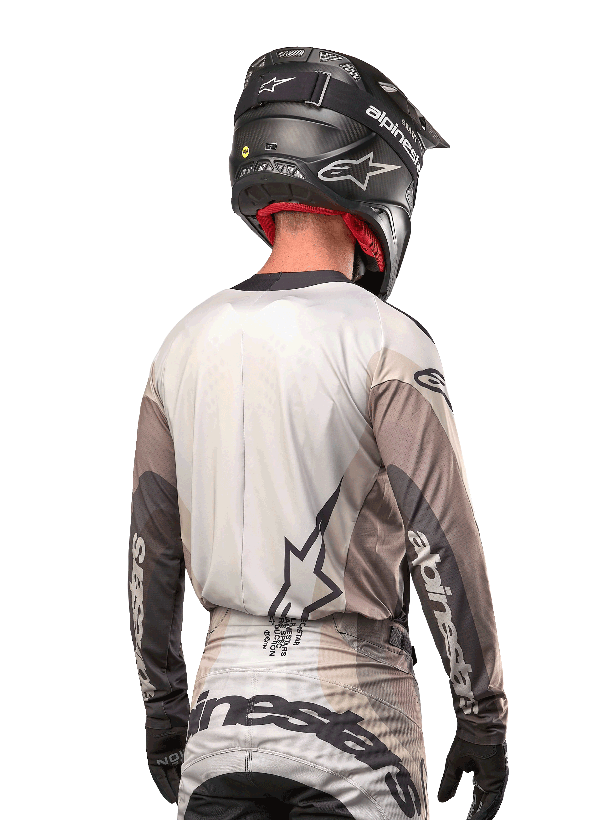 Piloto de motocross visto de trás a usar a camisola Alpinestars Techstar Pneuma 2024 em Dark Sand Iron Dust Gray, combinada com um capacete preto com acabamento em carbono, com um logótipo de estrela grande nas costas e a marca Alpinestars nas mangas.