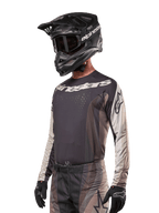 Alpinestars 2024 Techstar Pneuma Jersey, camisola de motocross, em areia escura e cinzento, top de performance de manga comprida com perfurações cortadas a laser e logótipo branco, usada com calças a condizer e capacete preto, corte atlético para condução todo-o-terreno
