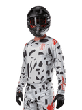 Camisola Alpinestars Techstar Rantera 2024, camisola de motocross, cinzento Haze Gray Camo com padrões abstratos pretos e detalhes vermelhos, design de manga comprida usado com capacete e luvas pretas a condizer, equipamento técnico de corrida todo-o-terreno