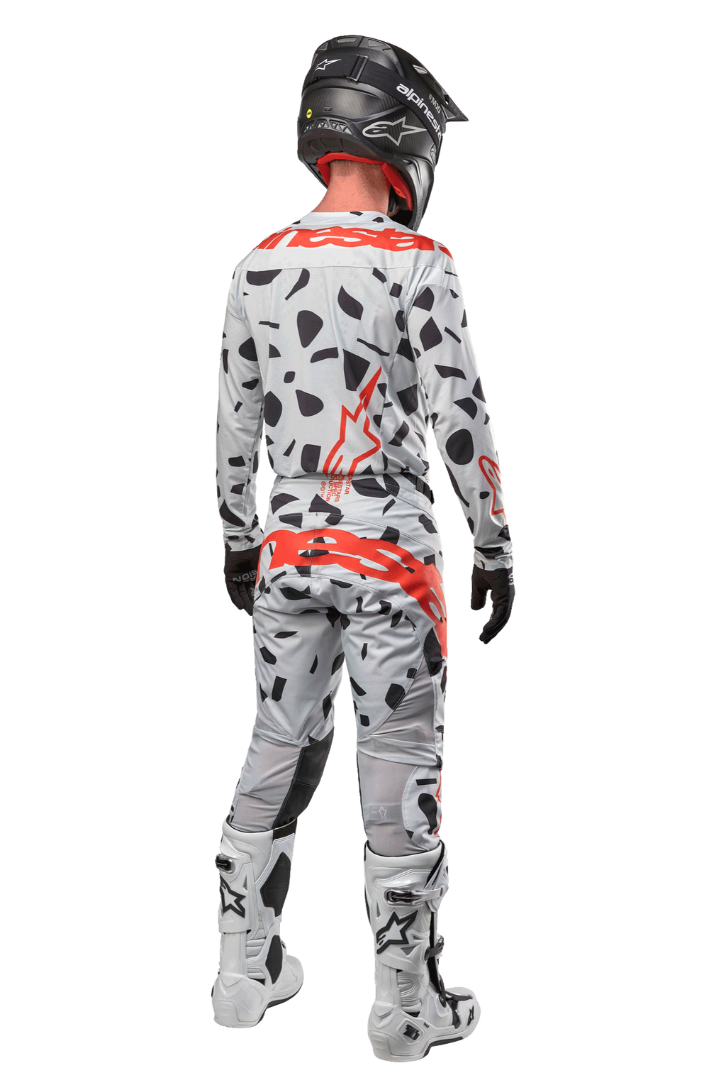 Piloto de motocross visto de costas a usar calças Alpinestars 2024 Techstar Rantera, camuflado cinzento (Haze Gray Camo) com manchas pretas e logótipos vermelhos, camisola a condizer, capacete preto e botas brancas, equipamento completo de corrida todo-o-terreno