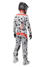 Piloto de motocross visto de costas a usar calças Alpinestars 2024 Techstar Rantera, camuflado cinzento (Haze Gray Camo) com manchas pretas e logótipos vermelhos, camisola a condizer, capacete preto e botas brancas, equipamento completo de corrida todo-o-terreno