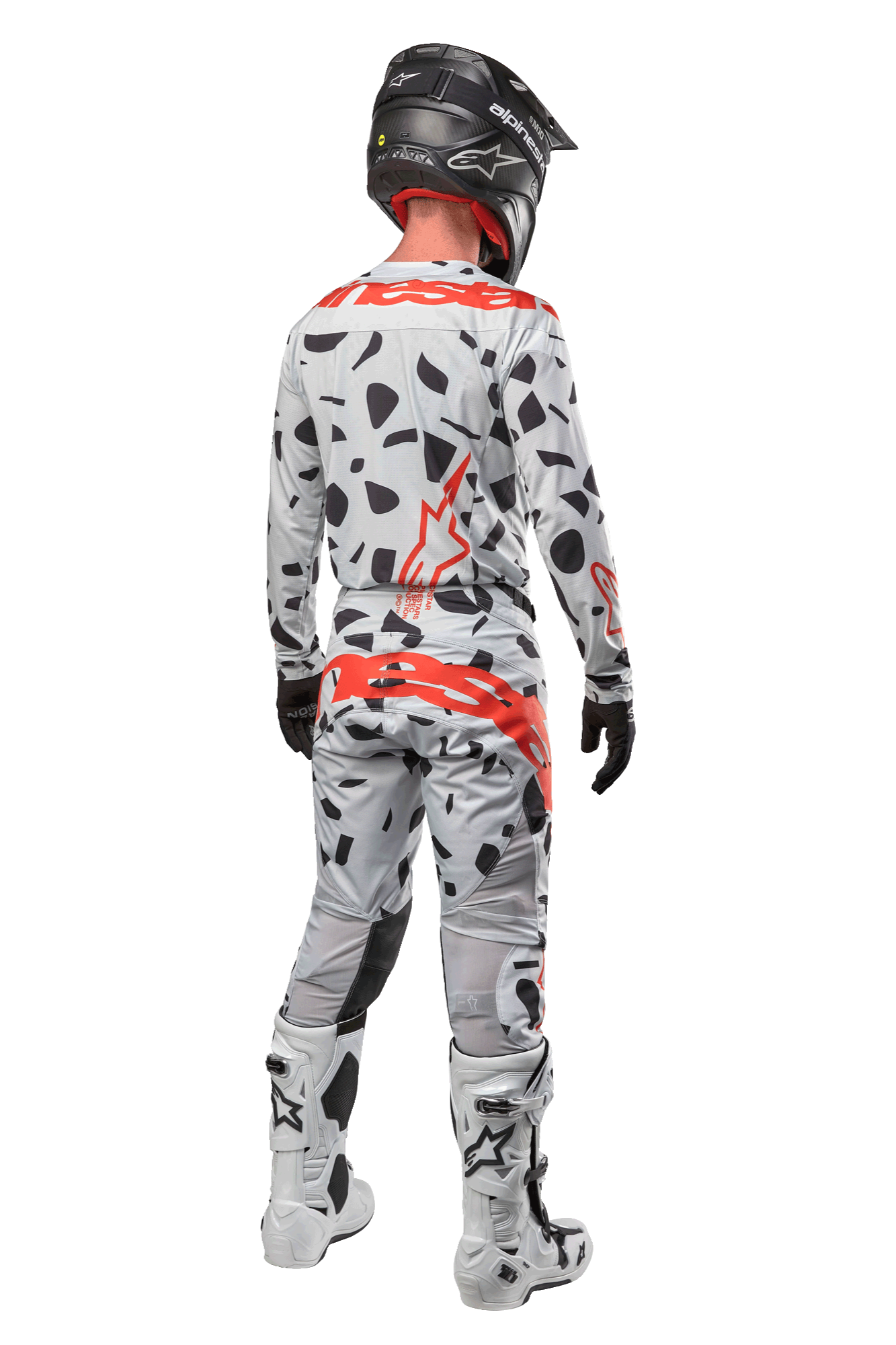 Piloto de motocross visto de costas a usar calças Alpinestars 2024 Techstar Rantera, camuflado cinzento (Haze Gray Camo) com manchas pretas e logótipos vermelhos, camisola a condizer, capacete preto e botas brancas, equipamento completo de corrida todo-o-terreno