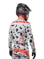 Piloto de motocross visto de costas a usar a camisola Alpinestars 2024 Techstar Rantera em Haze Gray Camo, com uma base cinza clara e manchas gráficas pretas, logótipos Alpinestars em vermelho vibrante nas costas e ombros, acompanhado por calças a condizer e capacete preto.